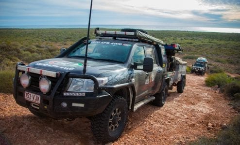 Toyota LandCruiser towing a caravan off-road on a rocky dirt track in the outback.