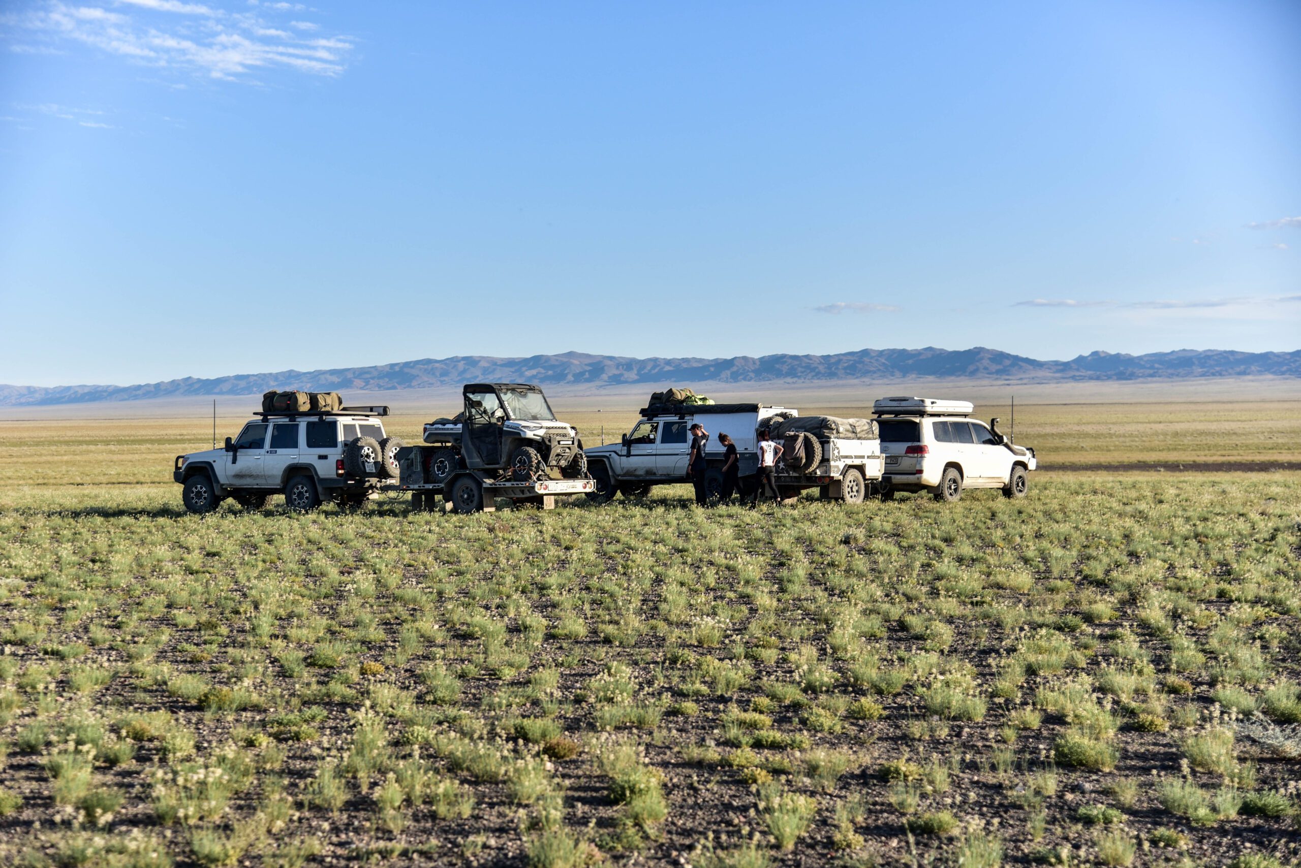 Convoy of 4WD vehicles parked on open grass plains with mountains in the background
