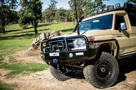 Toyota LandCruiser 78 Series Troop Carrier upgraded with TJM bull bar and off-road accessories, parked outdoors on rugged terrain.