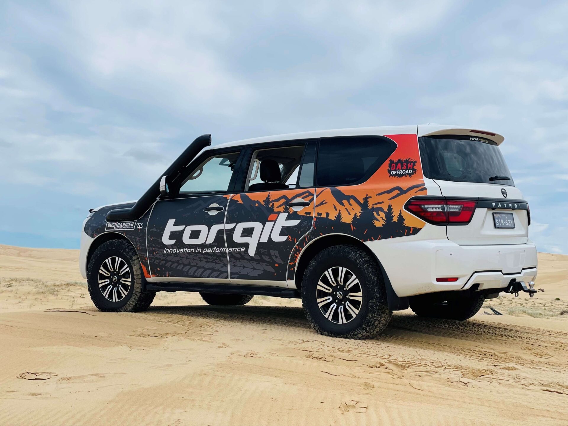 White Nissan Y62 Patrol with Torqit branding parked on sandy terrain under a cloudy sky.