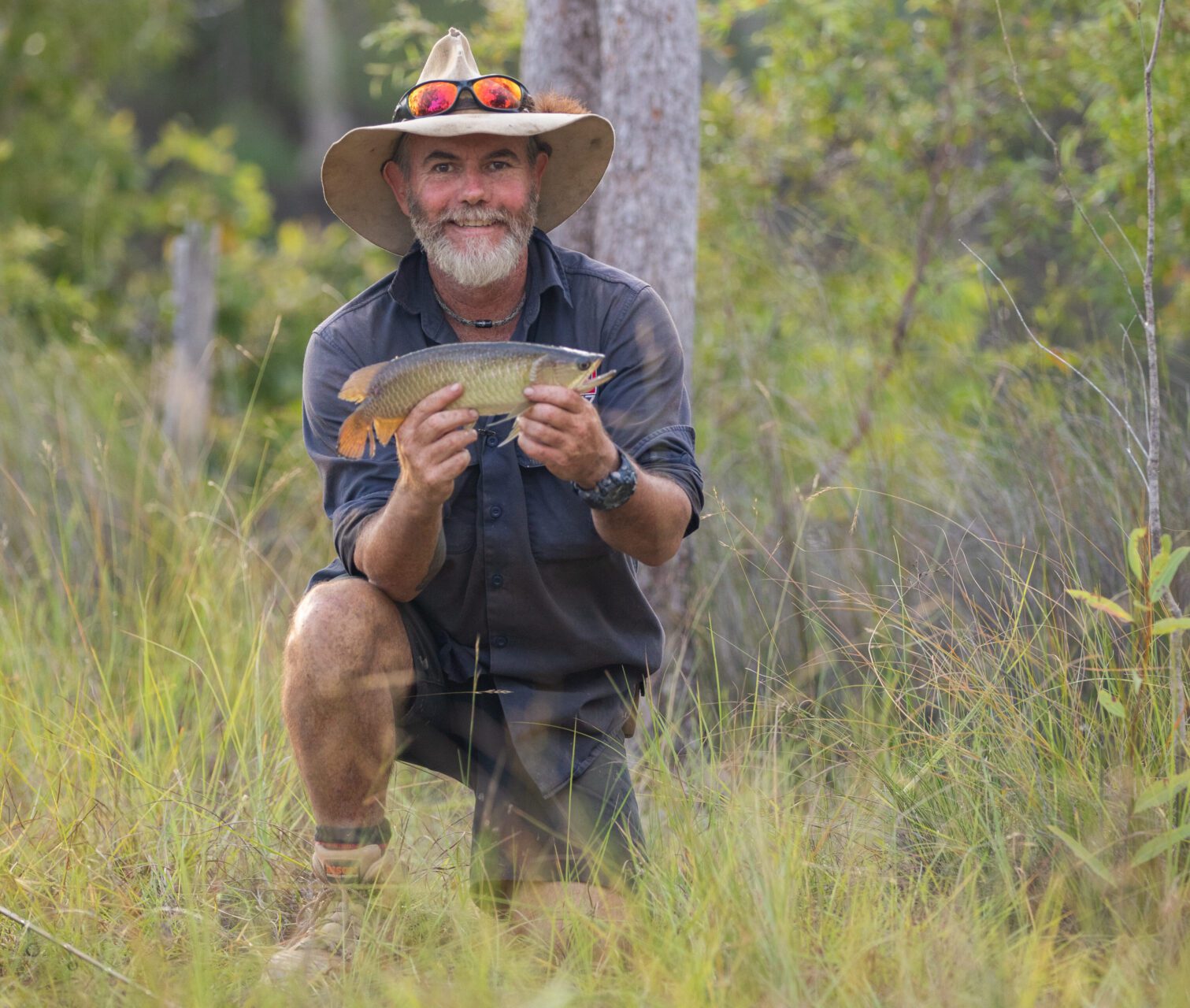 Graham Cahill kneeling outdoors holding a freshly caught fish in Dwellingup.