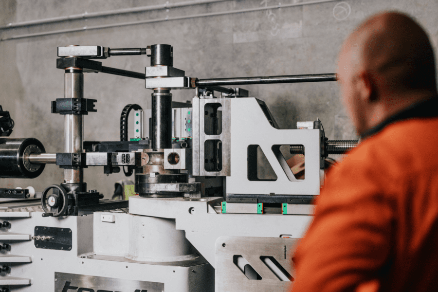Torqit mandrel bender machine in workshop with operator overseeing precision exhaust bending.