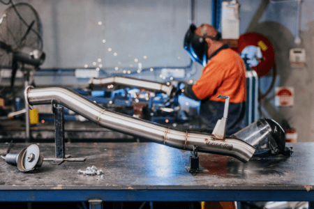 Welding a stainless steel exhaust system at Torqit workshop with sparks flying in the background.