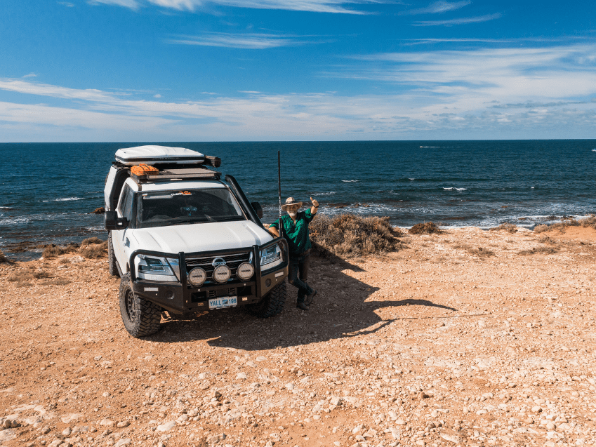 4WD parked on a coastal cliff in Western Australia with a person standing beside it, overlooking the ocean.