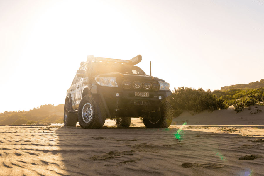 Toyota LandCruiser 200 Series driving on sandy dunes at sunset with off-road upgrades.