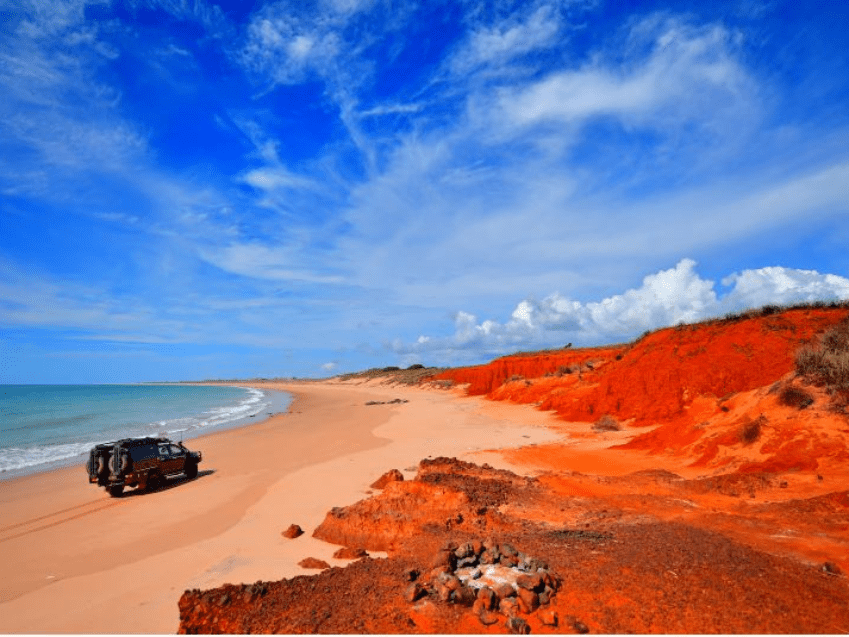 4WD driving along Cape Leveque beach with red cliffs, blue sky, and turquoise ocean